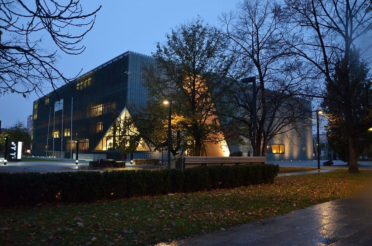 The glass facade of the POLIN Museum lit up at dusk